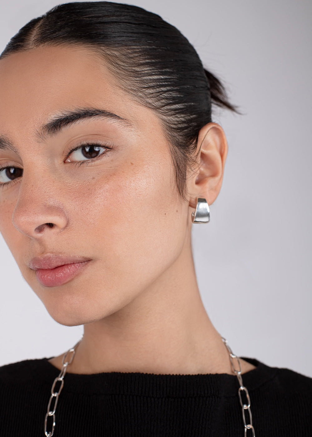 Close-up of a person wearing silver hoop earrings with a neutral background