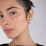 Close-up of a person wearing silver hoop earrings with a neutral background