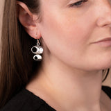 A close-up of a woman wearing a pair of silver dangle earrings shaped like stacked coffee cups, shown against her ear and neck.