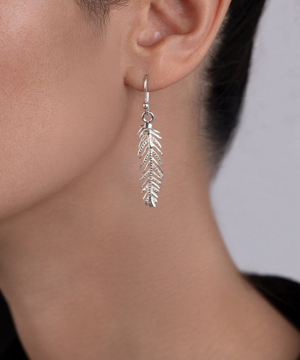 Silver leaf-shaped earring worn by a person against a neutral background