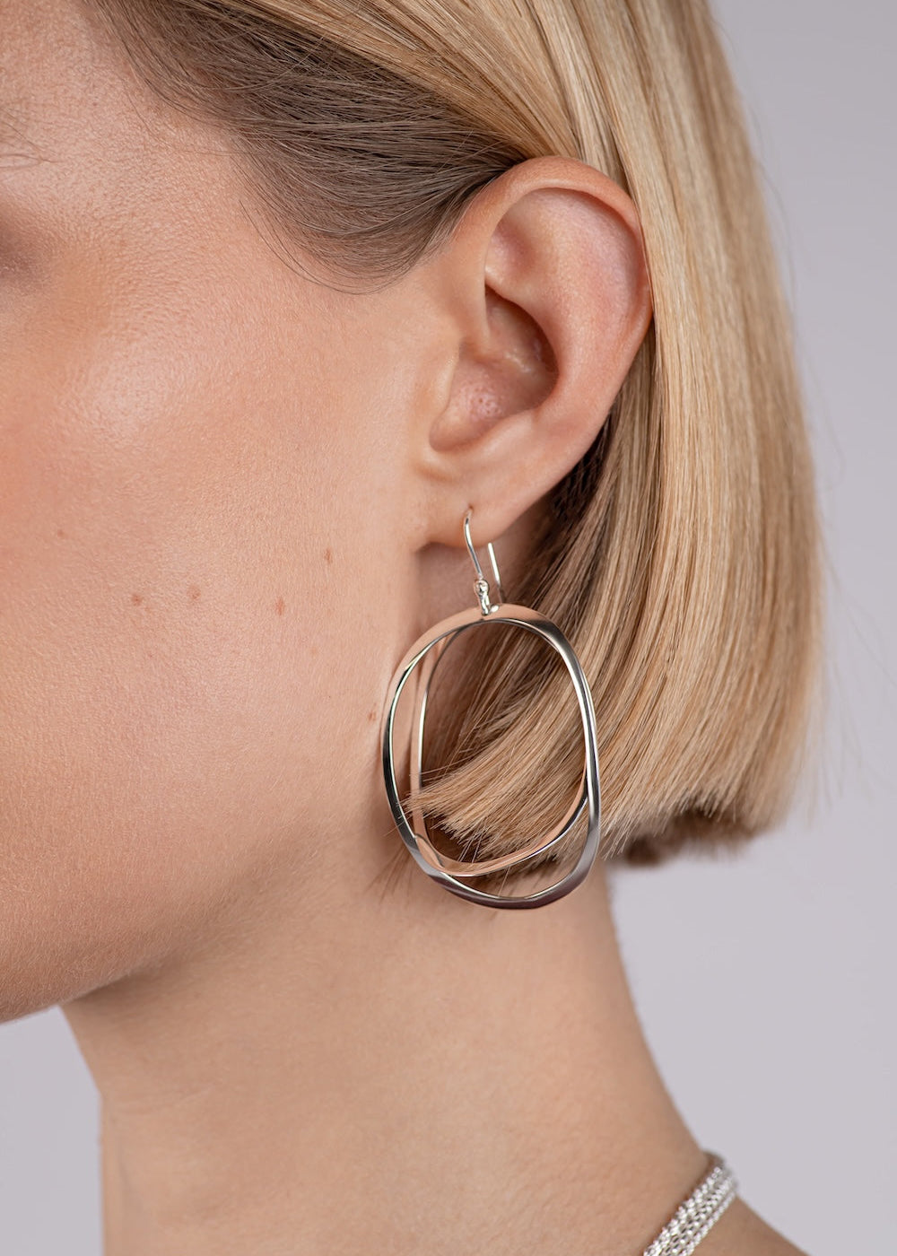 Close-up of a person wearing a silver hoop earring on a plain background