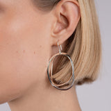 Close-up of a person wearing a silver hoop earring on a plain background