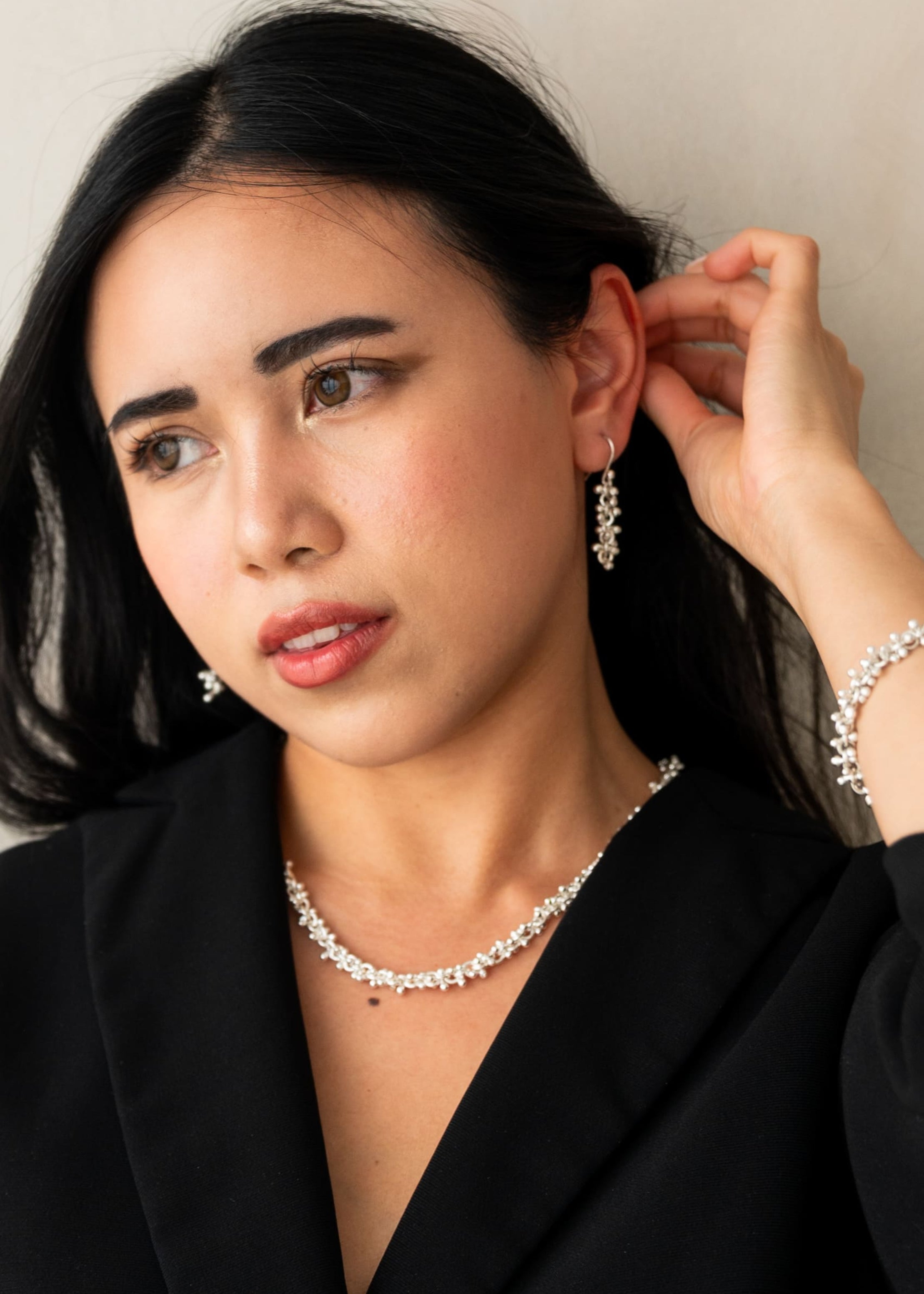 Woman wearing a black blazer and pearl necklace against a plain background