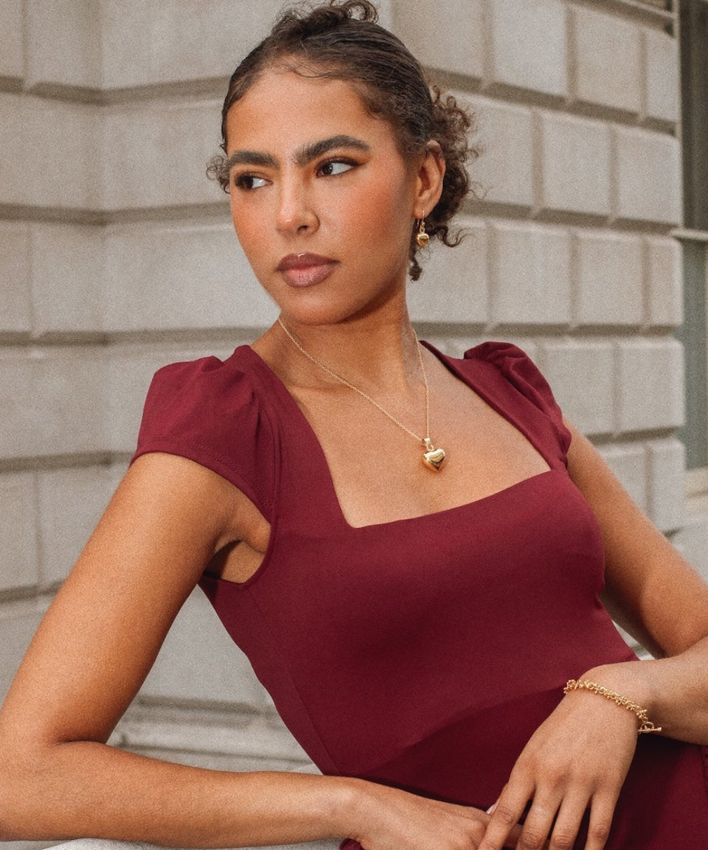 Woman in a burgundy dress standing against a stone building.