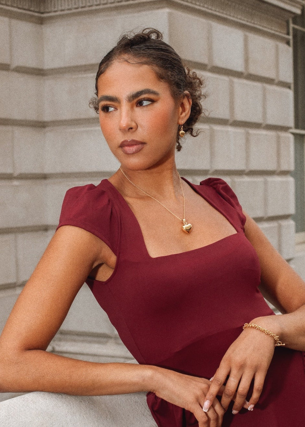 Woman in a burgundy dress standing against a stone building.