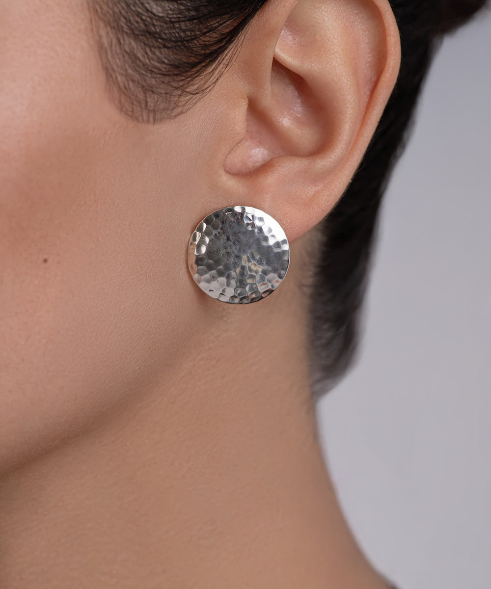 Close-up of a person wearing a silver round earring on a neutral background