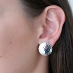 Close-up of an ear wearing a silver round earring with a sparkling gemstone.