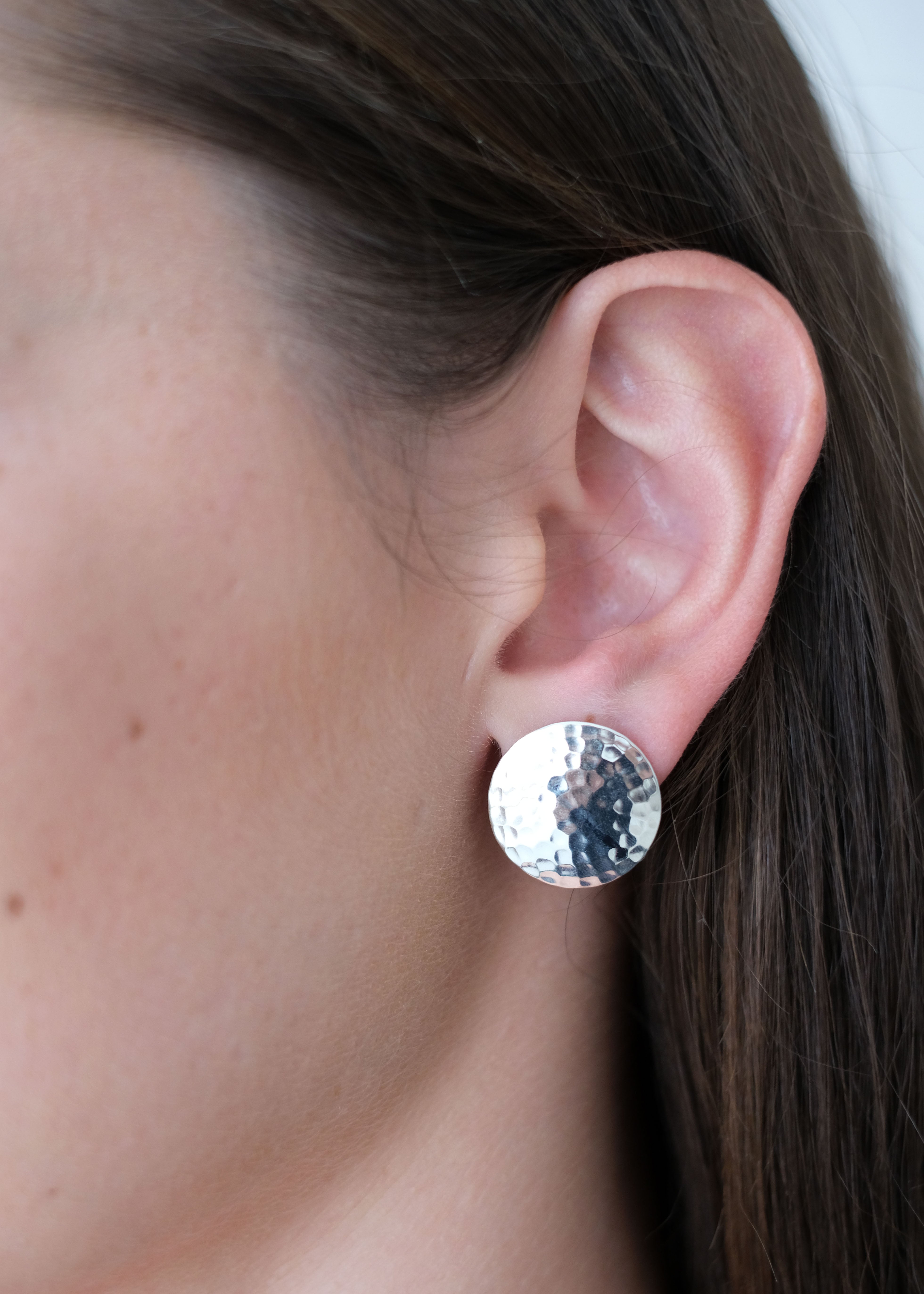 Close-up of an ear wearing a silver round earring with a sparkling gemstone.