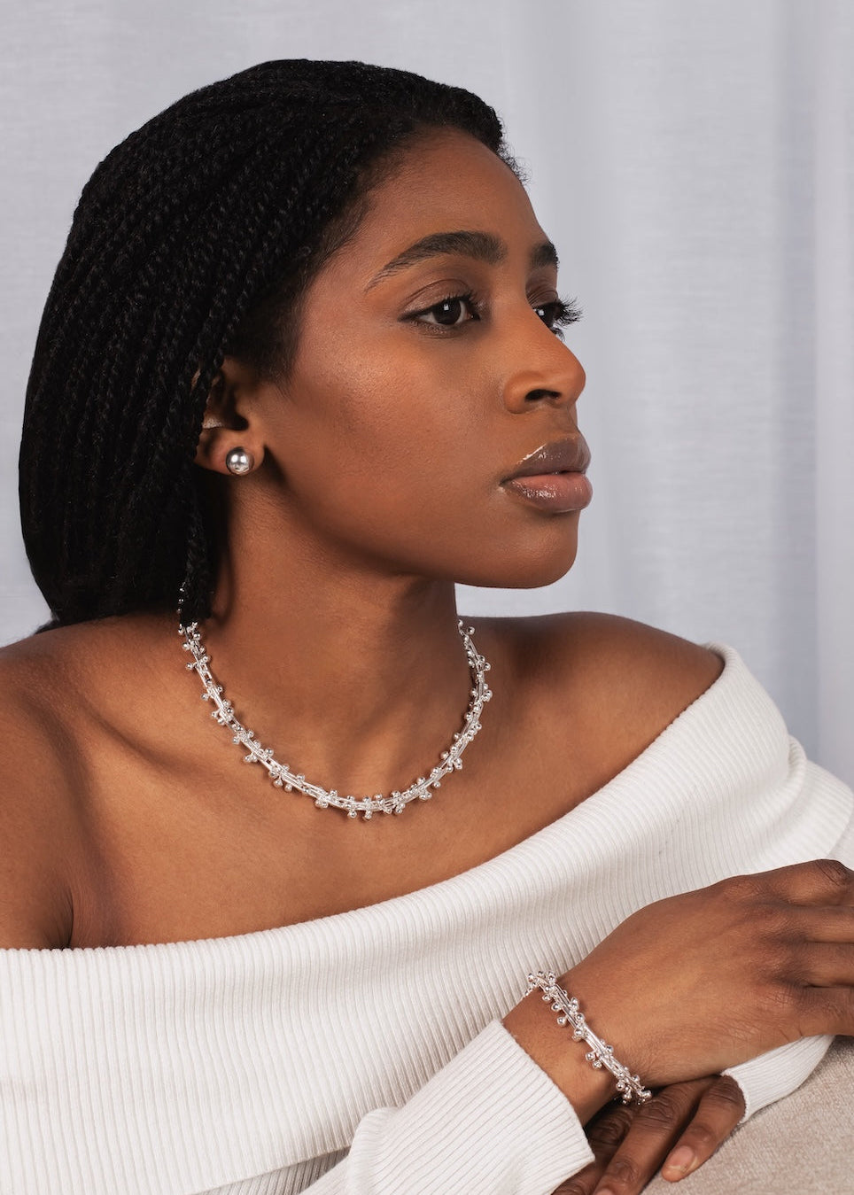 Woman wearing a white off-shoulder top and jewelry against a plain background
