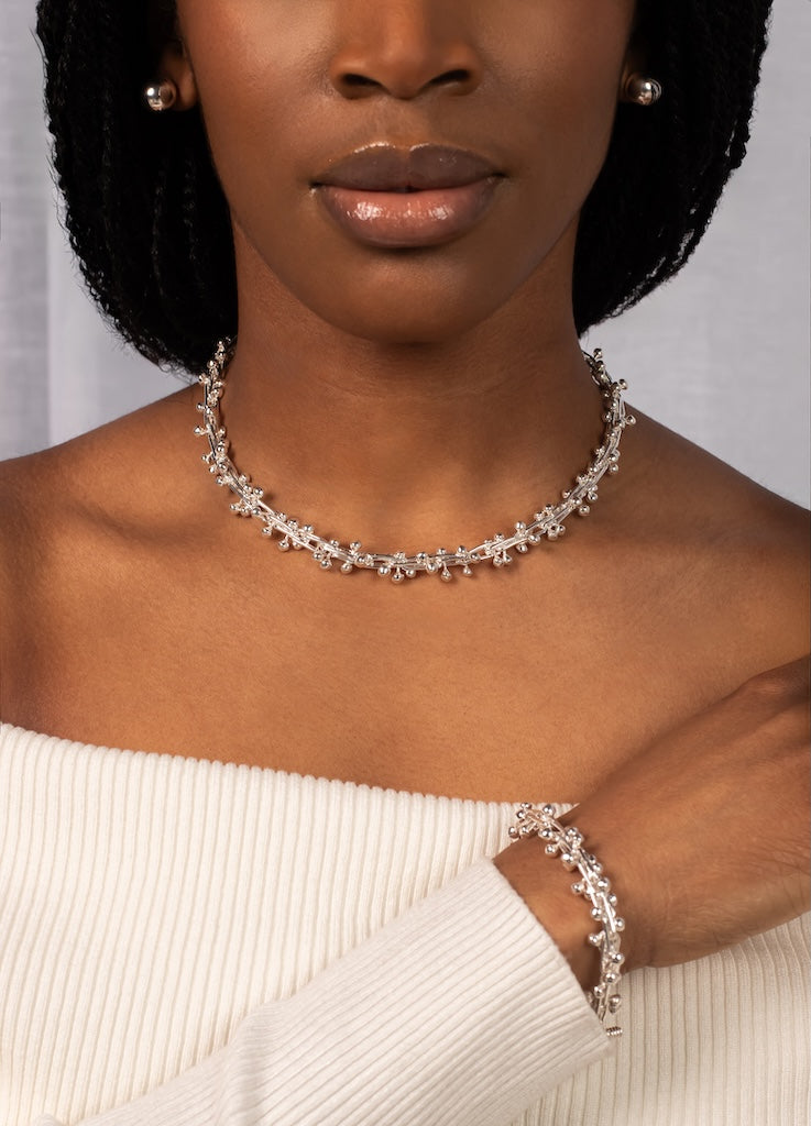 Woman wearing a silver necklace and bracelet against a neutral background