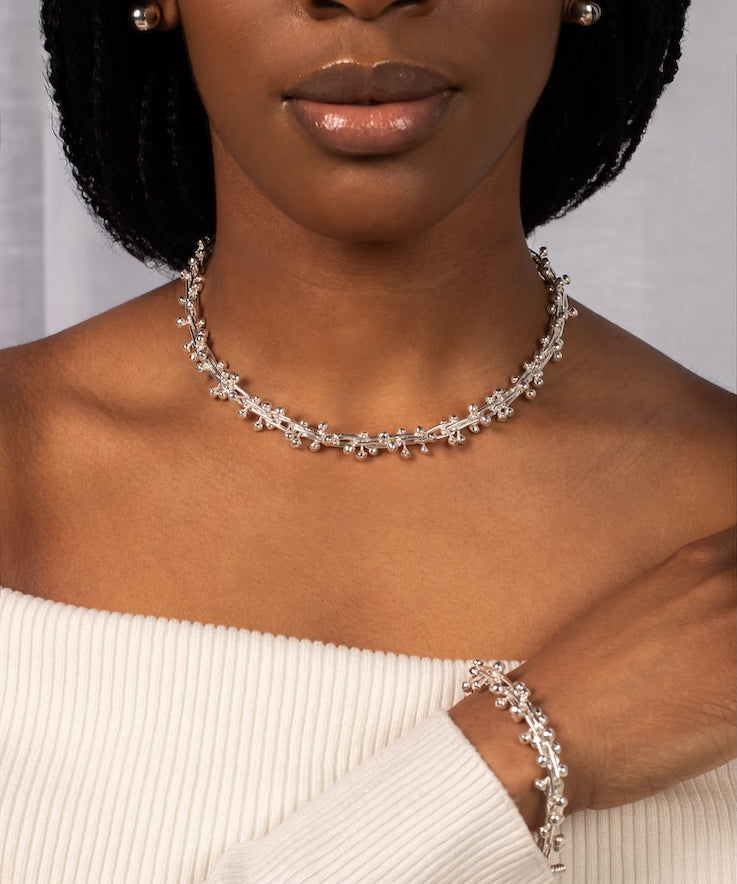Woman wearing a silver necklace and bracelet against a neutral background