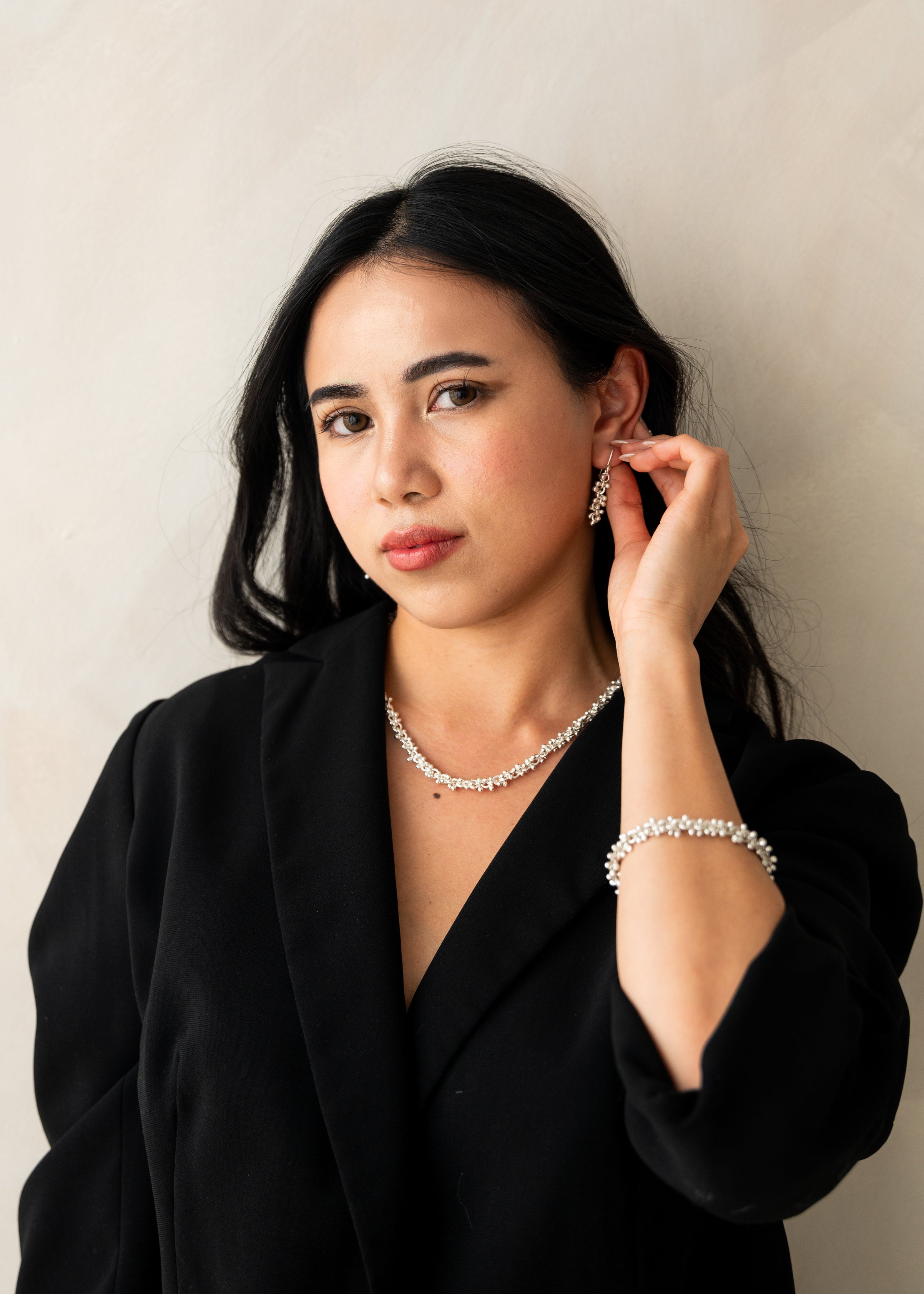 Woman wearing a black blazer and jewelry against a plain background