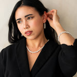 Woman wearing a black blazer and pearl necklace against a plain background