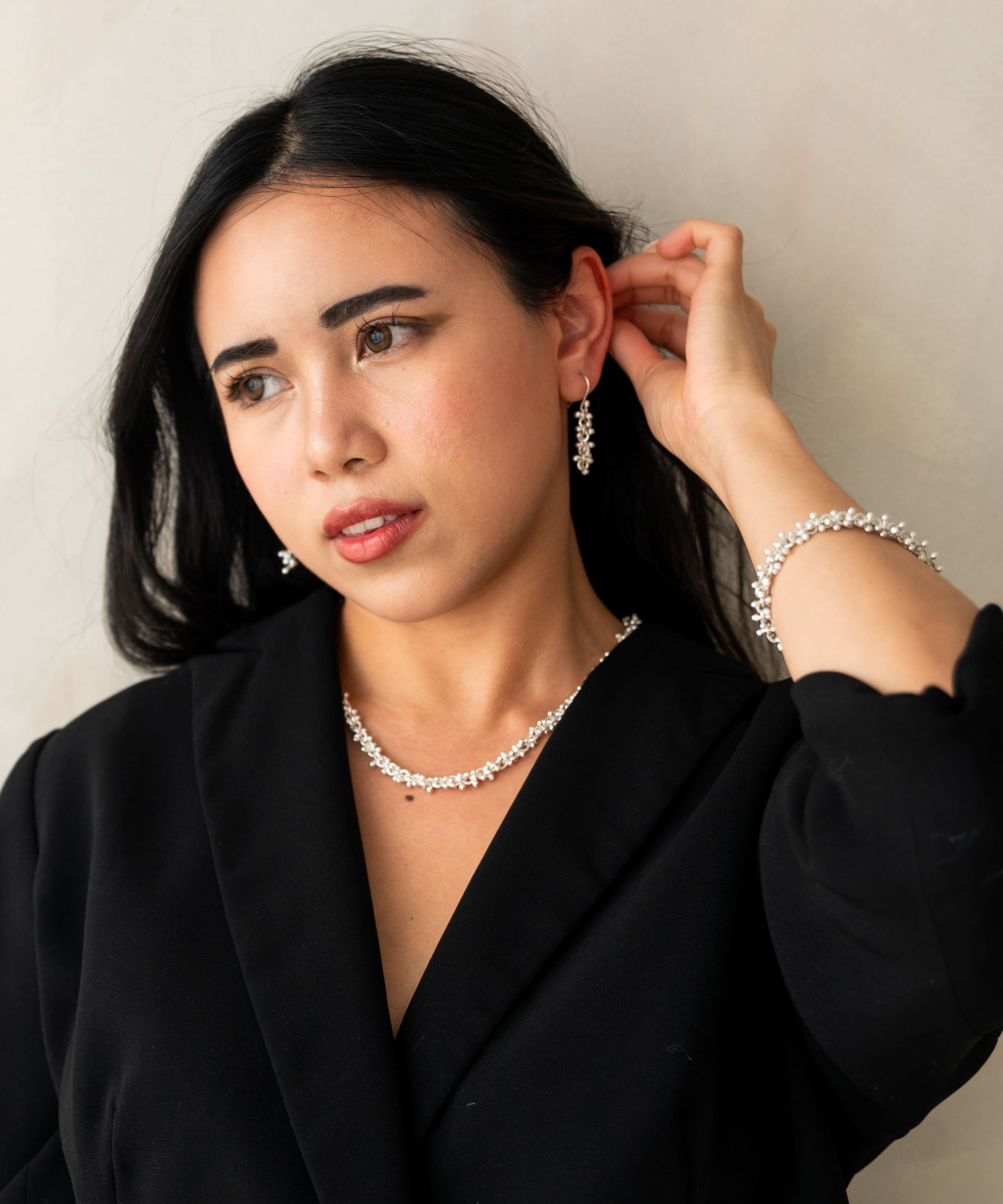 Woman wearing a black blazer and pearl necklace against a plain background