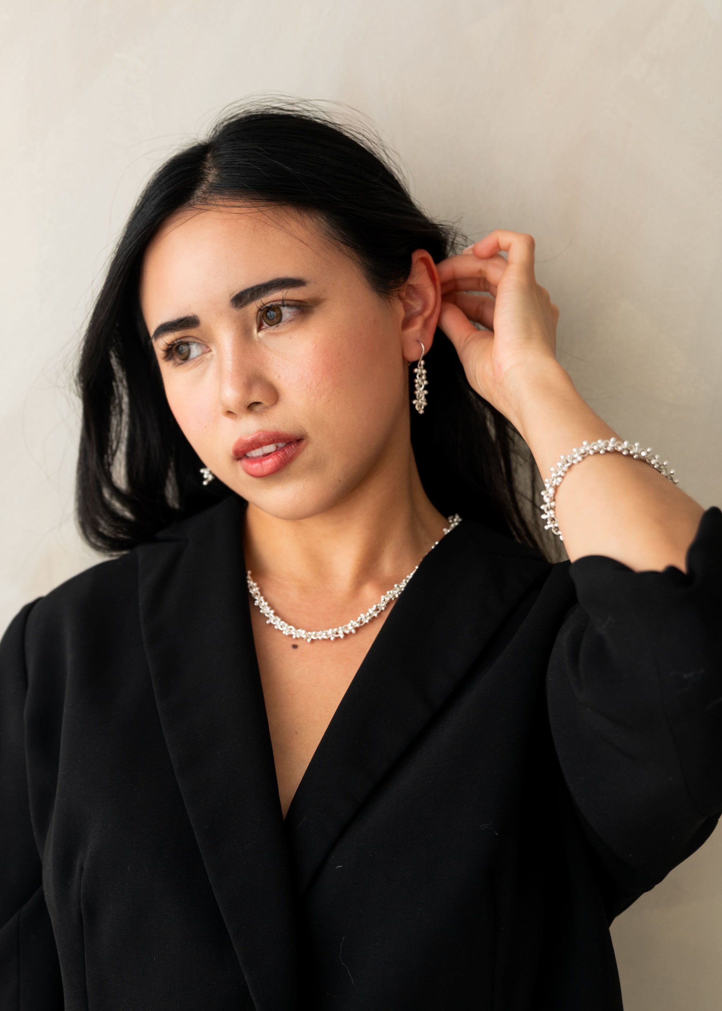 Woman wearing a black blazer and pearl necklace against a plain background